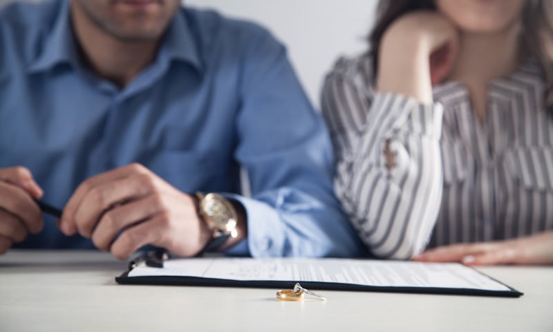 Couple sitting at a table with divorce papers and wedding rings in foreground, appearing distressed