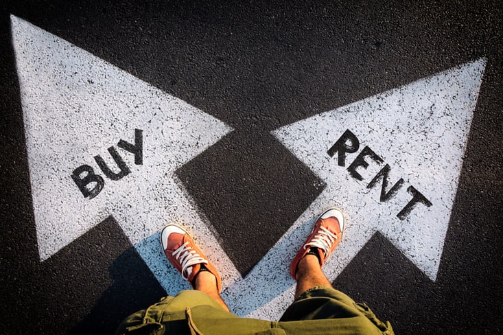 Persons feet in orange sneakers standing at intersection of white arrows painted on asphalt, with BUY and RENT text pointing in different directions