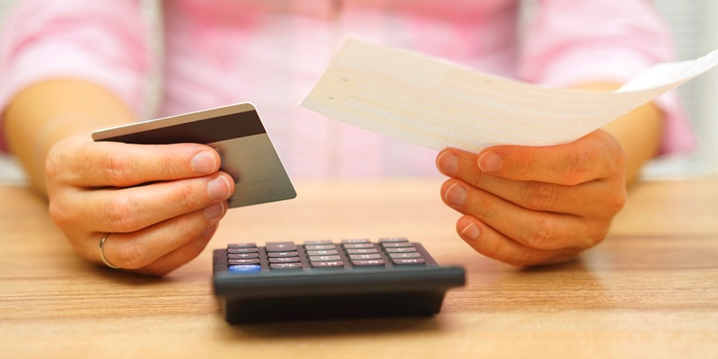 Man holding check and credit card over calculator on desk