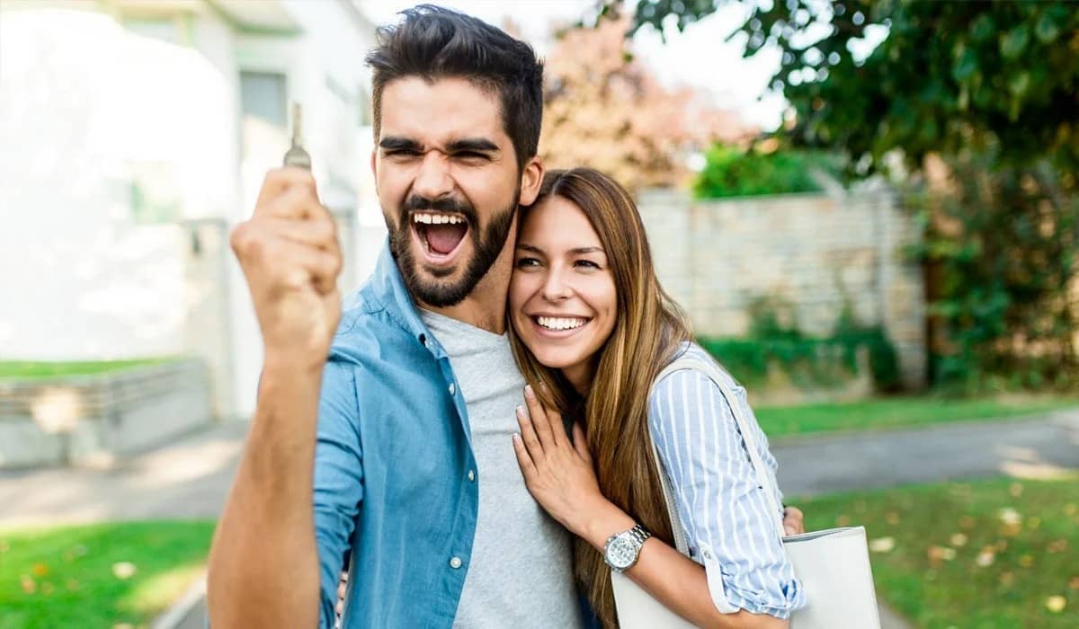 Happy young couple with key in hand standing outside in front of their new home