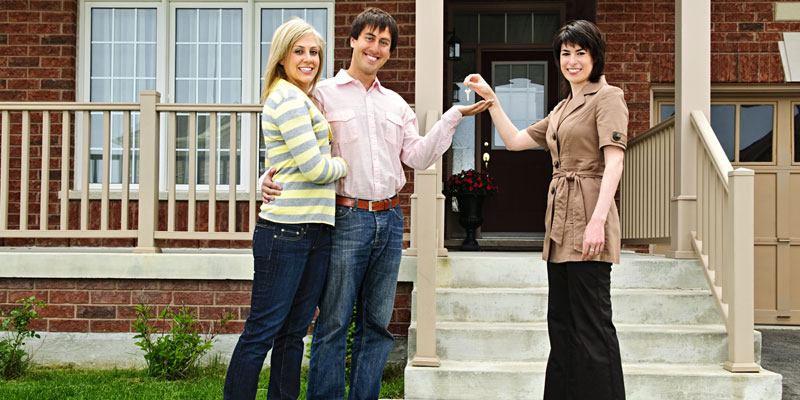couple holding up keys from real estate agent in front of new home